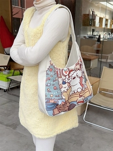 White canvas tote bag with cute cartoon bear print shown on shoulder in a cozy cafe setting