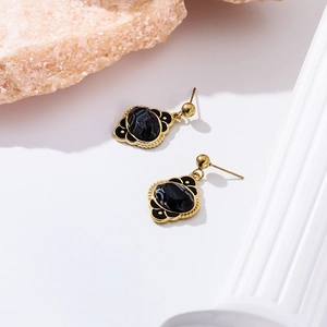 Detail of vintage gold-plated earrings with black marble enamel on a decorative stone base