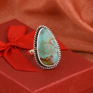Detalle de un anillo de turquesa en forma de gota con metal trenzado sobre caja de regalo roja