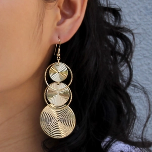 Macro shot of tiered gold metallic earrings with spiral texture on a female model