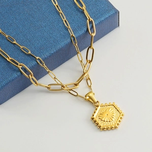 Close-up of golden double-layer necklace with sun pendant on a blue textured gift box