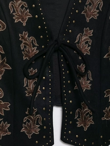 Close-up of vintage brown floral embroidery and gold studs on black V-neck vest