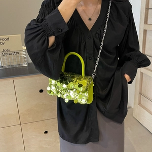 Detailed view of neon green sequin handbag with silver chain strap worn by a model