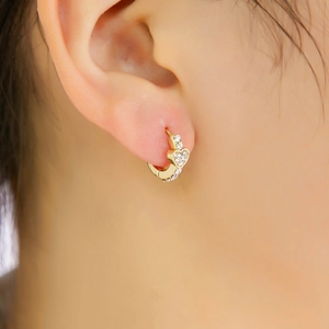 Gros plan d'une boucle d'oreille cœur dorée avec des strass brillants sur l'oreille