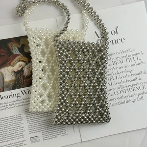 Close-up of handmade white pearl and silver metallic beaded phone bags on a magazine