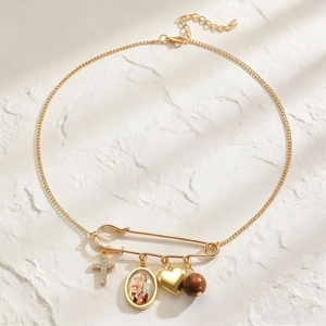Detail of golden safety pin pendant with cross, Virgin Mary medal, heart and wooden bead