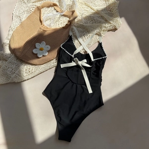 Detail of black one-piece swimsuit with white piping and criss-cross lace-up back design