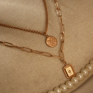 Detail of gold double-layer necklace featuring starburst coin and rhinestone square pendant