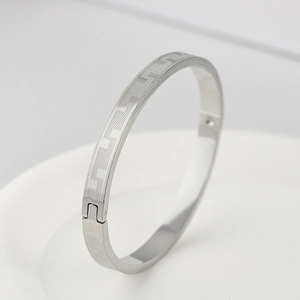Detail of silver stainless steel bangle featuring geometric Greek key pattern engraving