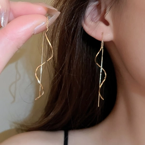 Close-up of golden wavy spiral threader earrings showing minimalist flowing metal design