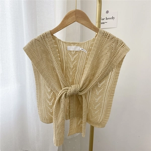Beige knitted shawl vest with cutout pattern and front tie design on a wooden hanger