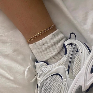 Detalle de una tobillera de cadena cubana dorada de 4mm llevada con zapatillas blancas y calcetines