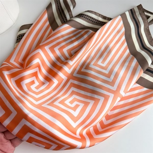 Gros plan d'un foulard carré en satin orange et blanc avec motifs géométriques de labyrinthe