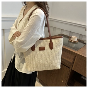 Detail of herringbone weave texture and brown leather strap on cream straw tote bag