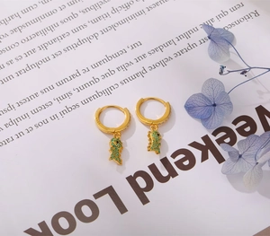 Detail of S925 silver golden dinosaur earring with green zircon on magazine background