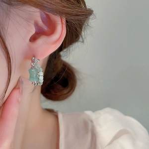 Detail view of silver earrings featuring green jade beads and bamboo-shaped stone pendant