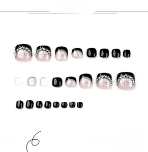 Detail view of black French toe nail set with white flower patterns and sparkling rhinestones