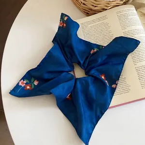 Navy floral silk hair scrunchie accessory displayed on an open book in a cozy setting