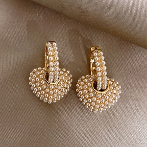 Dettaglio di orecchini a cuore placcati oro con perle su seta beige lussuosa