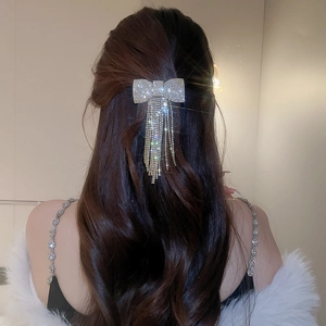 Détail d'une pince à cheveux nœud avec strass et pompon sur cheveux longs