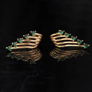 Detailed close-up of gold angel wing ear cuffs with green heart-shaped gemstones