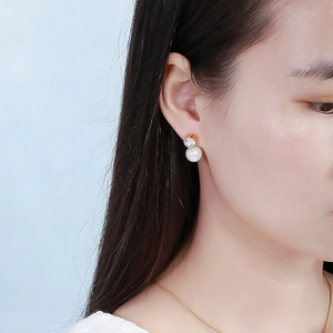 Dettaglio di un orecchino dorato con perla bianca e zircone indossato da una modella