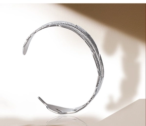 Macro detail of silver feather bracelet showing intricate texture and open-cuff design