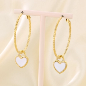Detail view of gold heart drop earrings with hammered texture on pink display stand