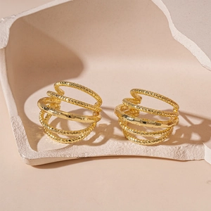 Detailed macro view of gold-plated multi-layer spiral earrings on a minimalist stone prop