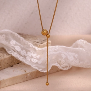 Detail of 18K gold-plated Y-shaped snake chain necklace with beads on marble surface