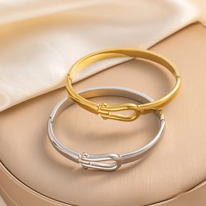 Macro shot of minimalist gold and silver horseshoe buckle bracelets on silk fabric