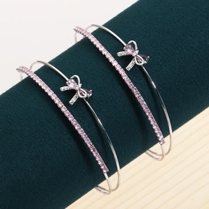 Silver bow bangle with pink zircon stones on green velvet display stand