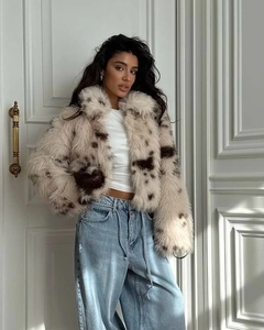 Detail of short faux fur coat with dark brown spots on cream base worn with denim jeans