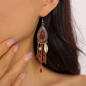 Close-up of golden teardrop earrings with red beads and long metal tassel fringe