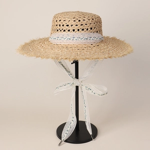 Detail of raffia straw hat with raw frayed edges and floral lace ribbon bow