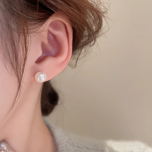 Close-up of elegant white round pearl stud earring worn on model's ear with soft glow