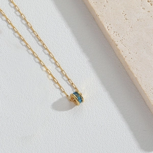Détail d'un collier doré avec pendentif cylindrique en zircon bleu sur cuir blanc
