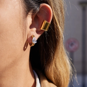 Golden C-shaped ear cuff and pear-cut zircon drop earring worn on female model's ear