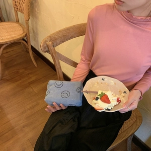 Blue corduroy makeup bag with embroidered smileys shown in a lifestyle coffee shop setting