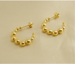 Detailed view of 18K gold beaded C-shape earrings on elegant beige silk fabric
