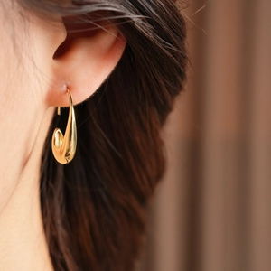 Close-up of minimalist 14k gold plated oval drop earring worn on model's ear