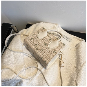Detail of green floral embroidery on straw bag with white leather handle and strap