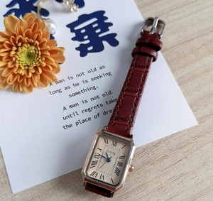 Close-up of vintage square watch with Roman numerals and brown leather strap on wooden desk