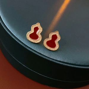 Detailed view of gold gourd earrings with red inlay and cubic zirconia on a green box
