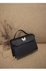 Detail of black mini flap bag with glitter finish and butterfly metal ornament on ivory base