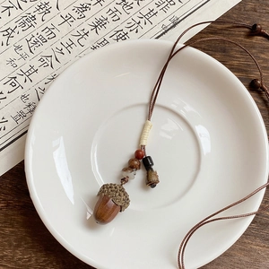 Close-up of a brown wood acorn pendant with rope chain on white ceramic dish