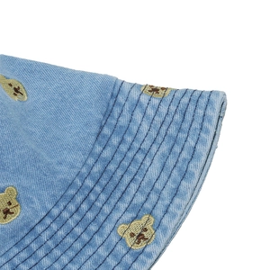 Close-up of light blue denim bucket hat featuring detailed brown bear embroidery