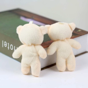 Vista trasera de dos mini ositos de peluche beige con lazos para colgar sobre un libro