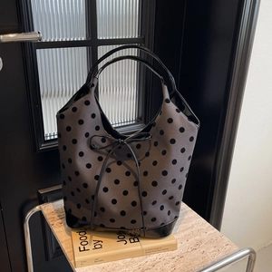 Polka dot knitted tote bag with shiny leather trim and drawstring bow on marble display