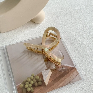 Macro shot of an elegant beige marble acetate and gold metal hair claw clip detail